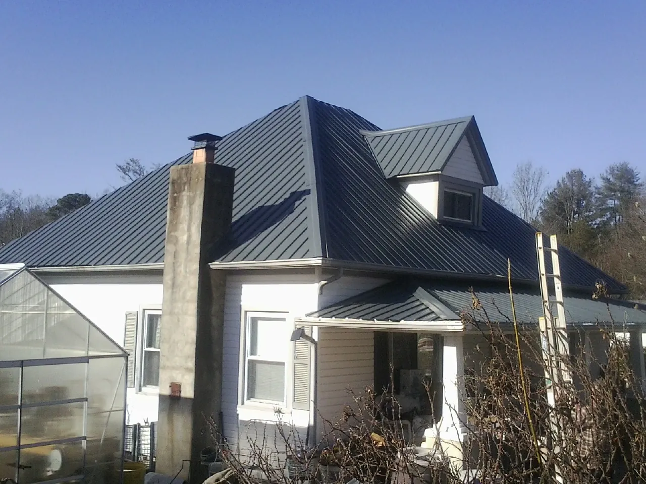 Dark blue standing seam metal roof on a white farmhouse with dormer — Slate & Tile Roof Repair by Roofing Brothers in Mineral Springs