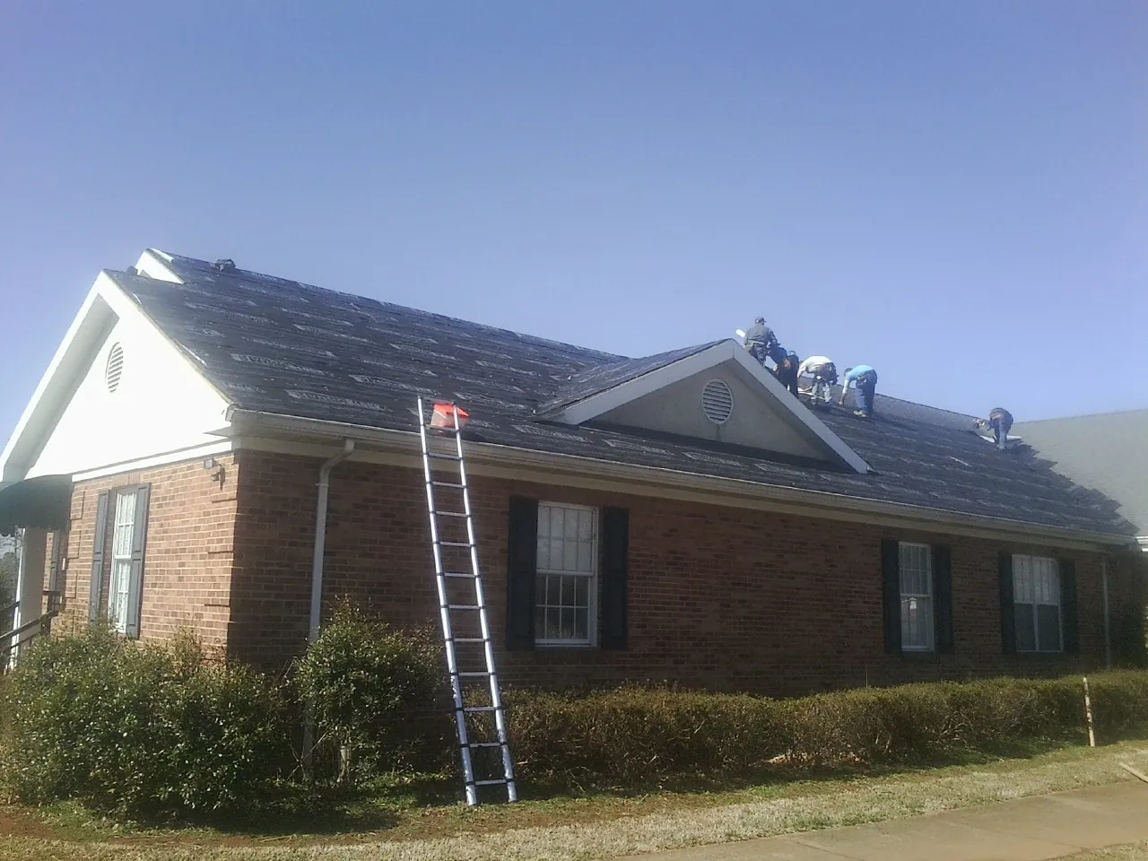 Crew tearing shingles off a brick ranch roof with a ladder set — Metal Roof Repair work by our crew in Mineral Springs