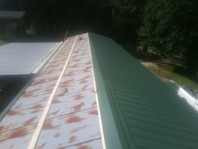 Old rusted panels beside newly installed green metal roofing — Wind Damage Roof Repair by Roofing Brothers in Mineral Springs