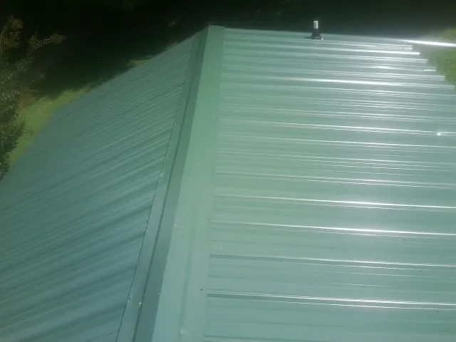 New green metal panels meeting at the ridge of a roof — Flat Roof Repair work by our crew in Mineral Springs
