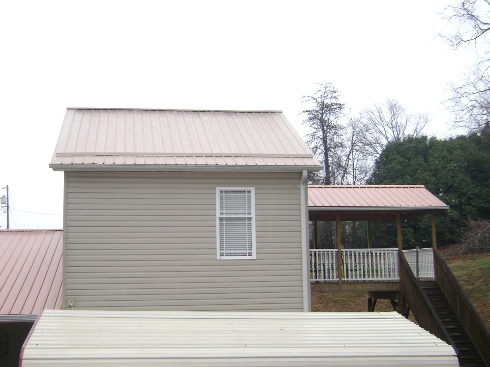 Tan metal roofs on a two story addition and attached porch, from a Roof Replacement job in Mineral Springs